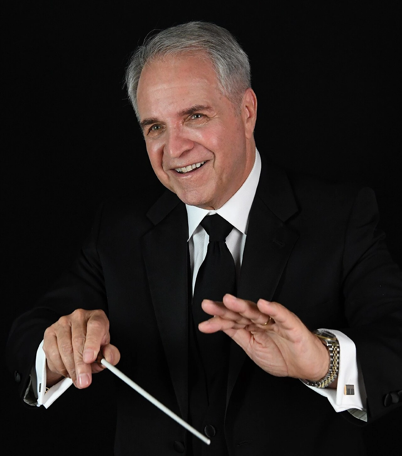 Charles Calello conducting, posed portrait against a black background