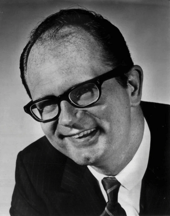 Black-and-white portrait of actor Charles Nelson Reilly smiling in glasses and a suit.