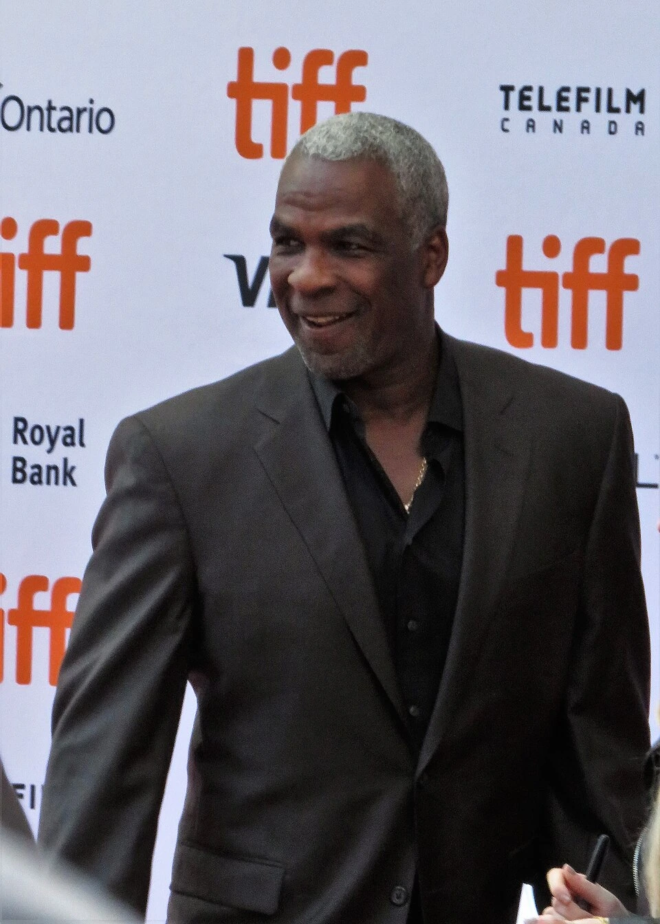 Charles Oakley smiling at an event in a dark suit against a branded step-and-repeat backdrop